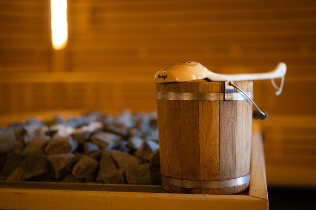Traditioneller Holzeimer mit Schöpfkelle vor heißen Steinen auf einem Saunaofen in der Ith Sole Therme.
