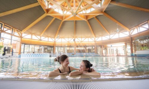 Zwei Frauen halten sich im Wasser, am Rand vom Bewegungsbecken der Ith Sole Therme fest und lächeln sich an.